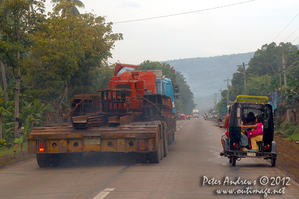 The low-loader truck is overtaking the trike as as its school-bound passengers look on. Along the highway to Kidapawan City, Davao del Sur Province, Mindanao, Philippines. Photo copyright Peter Andrews, Outimage Australia.