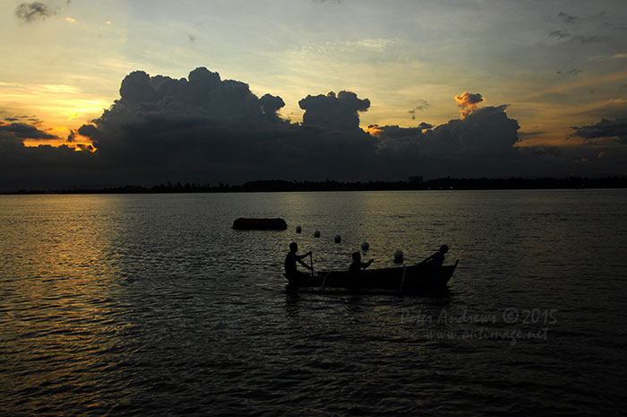 Three boys paddling a small outrigger boat just off Paradise Island Beach on Samal Island.