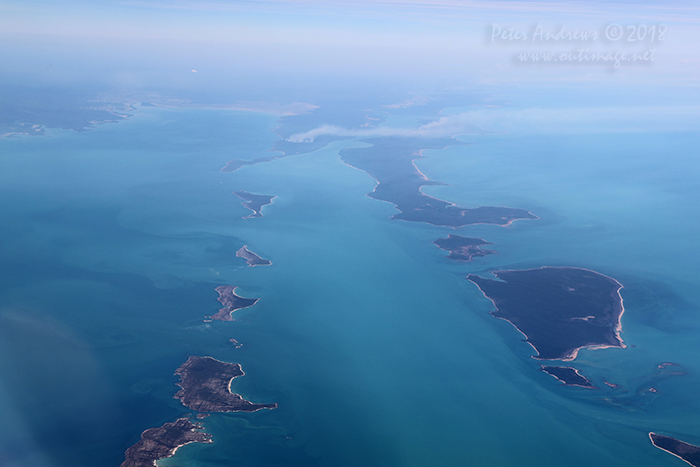 Flying out towards the Arafura Sea over the Cunningham Islands of Jirrgari, Bumaga, Warnawi, Alger on the left; Drysdale, Graham and Elcho Islands which form the the Wessel Island Group on the right. This is the coast of East Arnhem Land which is home of the Yolngu People, near Nhulunbuy in the Northern Territory. Traditional fire stick burning, an indigenous fire management practice is seen in the distance on the mainland and on Elcho Island. 11°35'56.7"S 136°08'25.5"E. High altitude shots from a flight between Sydney Australia and Manila, Philippines.