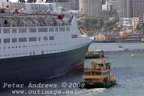 The passenger ferry Friendship slips past the Queen Elizabeth 2 in, Circular Quay Sydney with Luna Park and the North Shore skyline in the background.