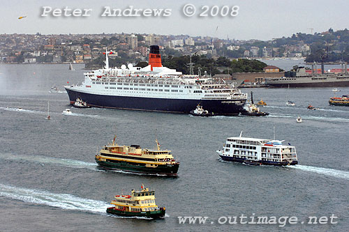 Queen Elizabeth 2 steaming out of Sydney Harbour in company of various working vessels on the harbour.
